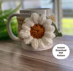 a crocheted coffee cup with a white flower on the inside and green leaves in the outside