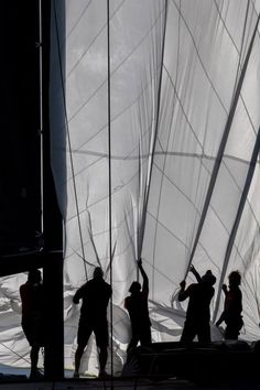 silhouettes of people working on a sailboat in the water with white fabric covering it