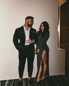 a man and woman standing next to each other in front of a white wall wearing black