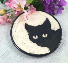 a black and white plate with a cat's face painted on it next to flowers