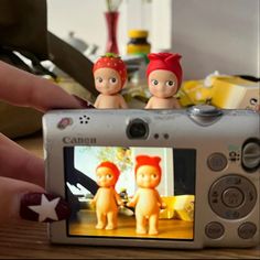 a person holding up a camera with two small dolls on top of the camera's screen