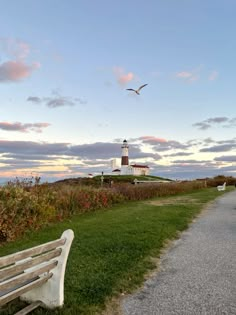 a bench sitting on top of a grass covered field next to a light house with a bird flying over it