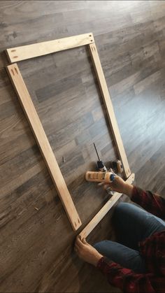 a person sitting on the floor with some tools in front of him and an unfinished frame