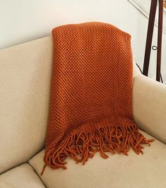 an orange knitted throw sitting on top of a couch next to a stair case