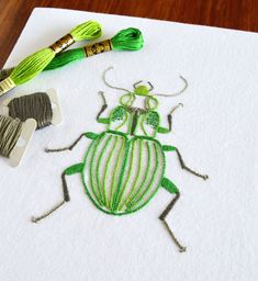 a green bug is sitting on a piece of paper next to some thread and two crochet hooks