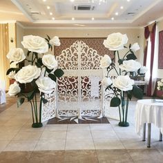 white roses are arranged in vases on the floor next to a wall with an intricate screen