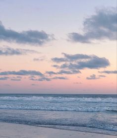 two people walking on the beach with surfboards under a cloudy blue and pink sky