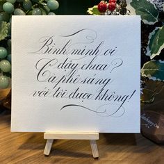 a white card with black writing on it sitting on a wooden easel next to a potted plant