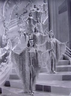 vintage black and white photo of women dressed in costumes on stairs with chandeliers