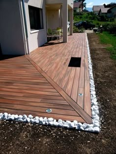 a wooden deck in front of a house with white pebbles on the ground and gravel around it