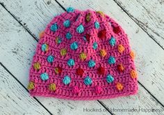 a pink crocheted hat with multicolored pom poms on it