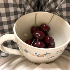 a white bowl filled with cherries on top of a checkered tablecloth cloth