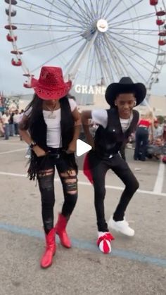 two people are dancing in front of a ferris wheel at an outdoor event, one is wearing a red cowboy hat and the other wears black