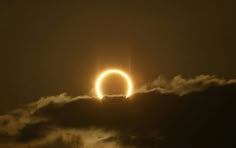 the solar eclipse is seen through clouds as it passes in front of an orange ring