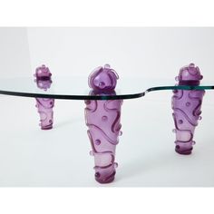 a glass table with three purple vases sitting on it's legs and one is upside down