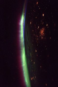 an airplane wing is lit up green and purple in the night sky as seen from space