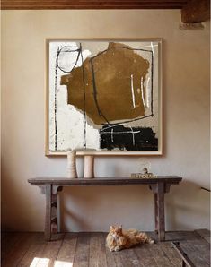 an orange cat laying on the floor in front of a large abstract painting hanging above a wooden table