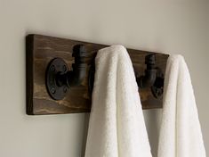 two towels hanging on the wall next to a towel rack with hooks and an iron pipe