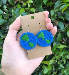 a pair of blue and green crocheted earrings with leaves on them sitting in front of a tree