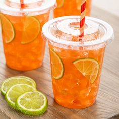 three cups filled with orange juice and limes on a wooden table next to two slices of lime