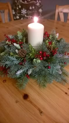 a candle is lit on top of a table with greenery and holly wreaths