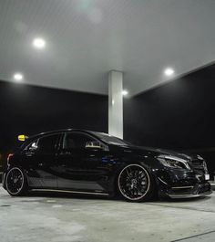 a black car parked in front of a gas station at night with lights on the ceiling