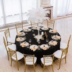 a black table topped with white chairs next to a tall vase filled with flowers and feathers