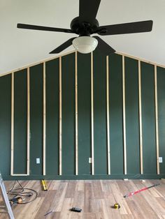 a ceiling fan in the middle of a room with green walls and wood flooring