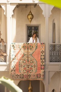 a woman is holding up a quilt in front of a building with balcony railings