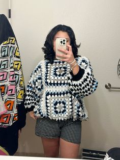 a woman taking a selfie in front of a mirror wearing shorts and a sweater