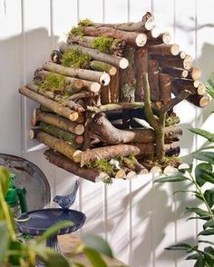 a bird house made out of wood and logs is hanging on the wall next to a potted plant