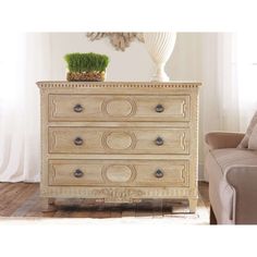 a white dresser sitting in a living room next to a couch and chair with a plant on top of it