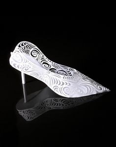 white high heeled shoes with intricate designs on the heels are lit up against a black background