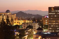 the city is lit up at night with mountains in the background