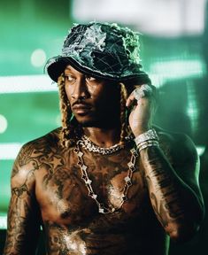 a man with tattoos and a hat on talking on a cell phone in front of a green background