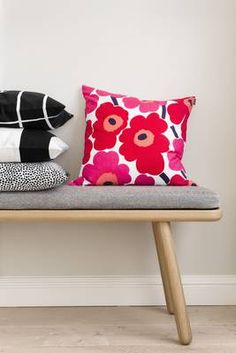 three pillows sitting on top of a bench next to a vase with flowers in it