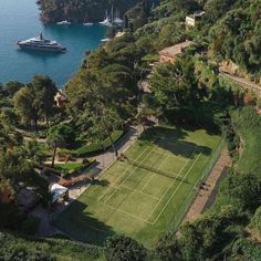 an aerial view of a tennis court surrounded by trees and water with a boat in the background