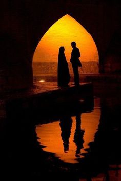 two people are standing in an archway at sunset