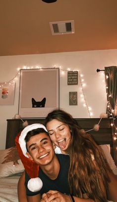 a man and woman laying in bed with christmas lights on the wall above their head