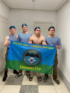 four shirtless men standing in a hallway holding a blue and green flag