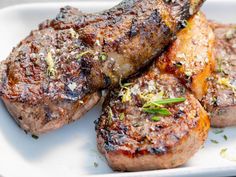 three steaks on a white plate with herbs