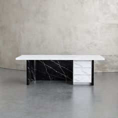 a black and white marble table with two drawers on it's sides, in front of a concrete wall