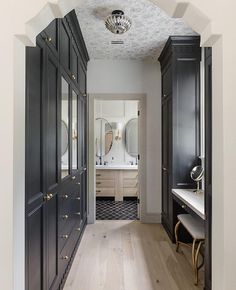 a long hallway leading to a bathroom with black cabinets and mirrors on both sides of the room