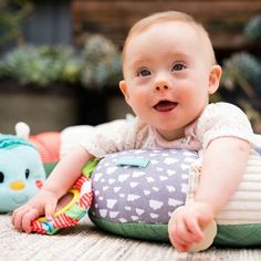 a baby laying on the ground with a stuffed animal in it's lap and smiling