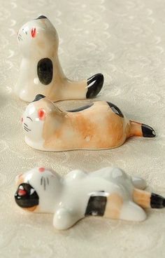 three ceramic cat figurines sitting on top of a white cloth covered tablecloth