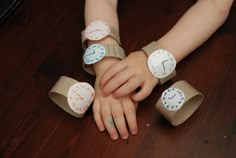 a child's hands with four different paper clocks on their wristbands, sitting on a wooden floor