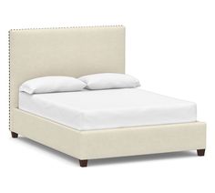 an upholstered bed with white sheets and pillows