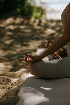 a woman sitting in the sand doing yoga on her stomach and arms with both hands