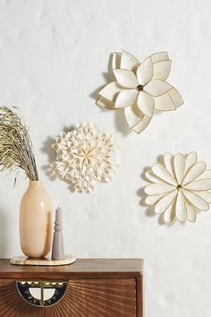 three decorative flowers are mounted on the wall above a dresser with vases and other items