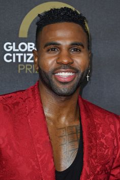 a man in a red jacket smiling at the camera with tattoos on his arm and chest